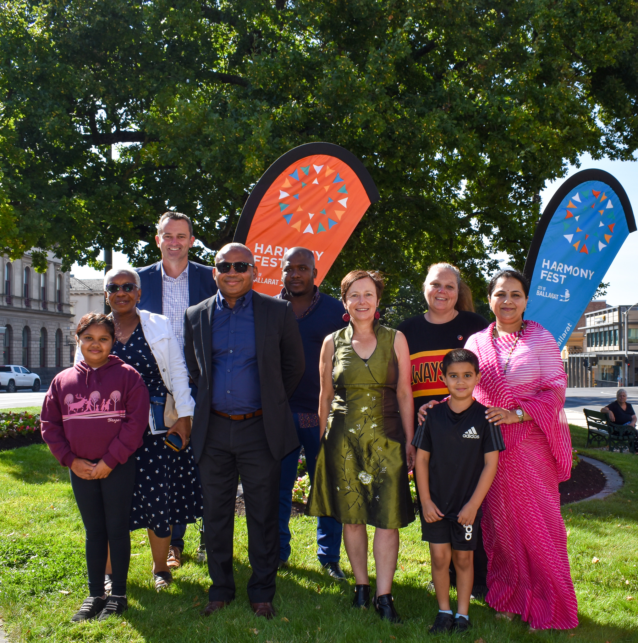 Group of people including Mayor Cr Daniel Moloney and Cr Coates along with Intercultural ambassadors in front of Harmony Fest banners