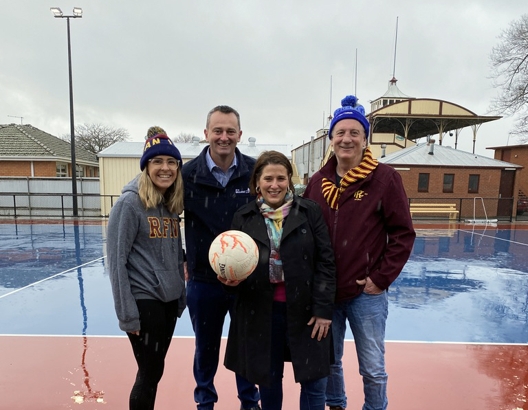 netballer, Mayor, Local Minister and President of Redan Football Club stand with a netball in front of the brand new netball courts and lights at City Oval
