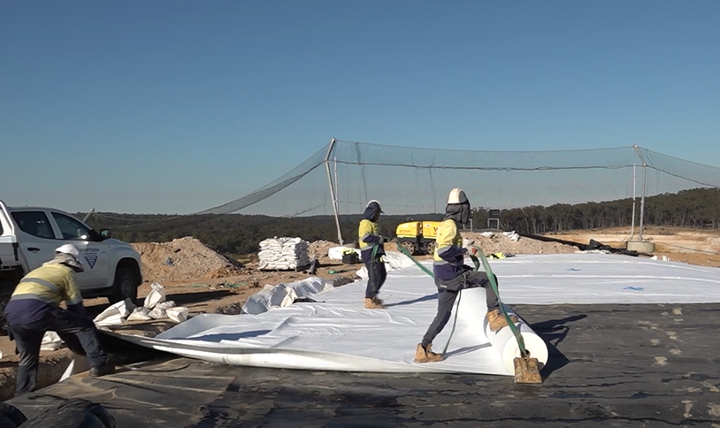 Workers roll out geotextile material at the landfill