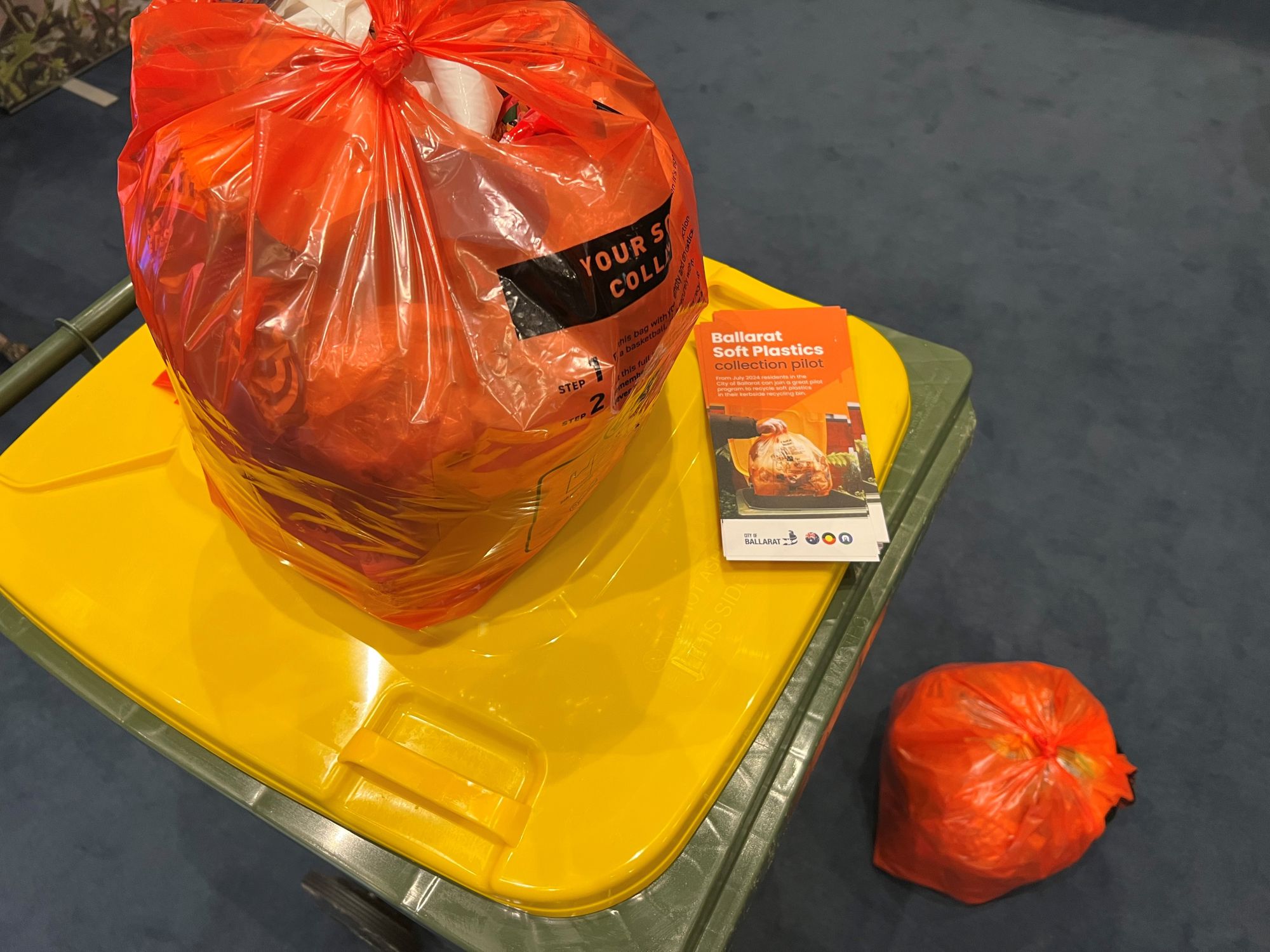 A soft plastics bag sits on top of the recycling bin