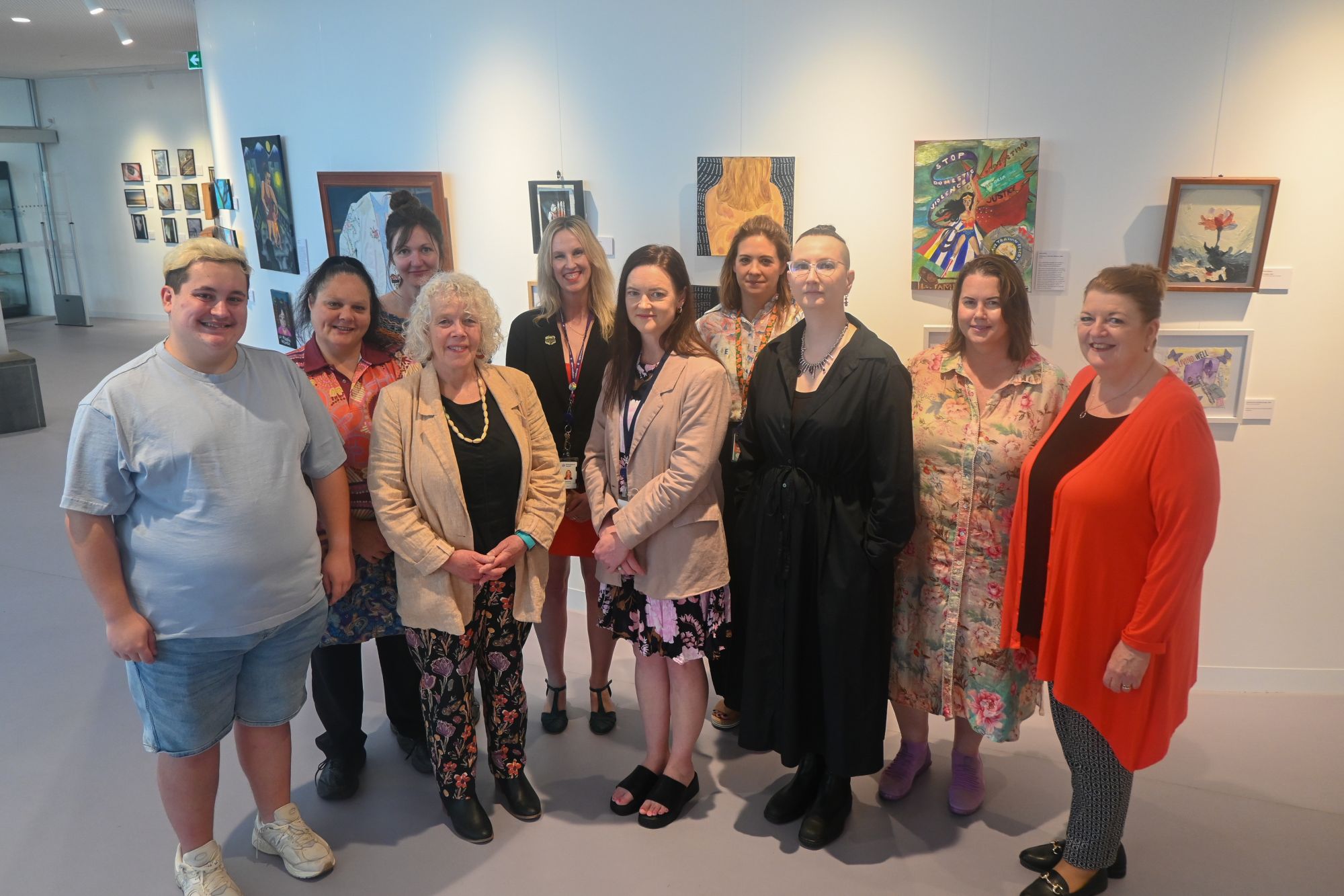 A group of people stand in front of a white wall covered with different pieces of art. 