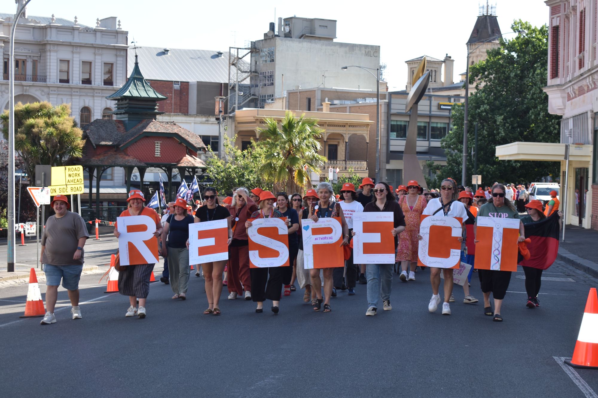 People holding banners spelling out 'Respect' walk down a street with a crowd of people following them.