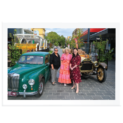 The mayor standing with two shop owners in the new bridge mall with some vintage cars