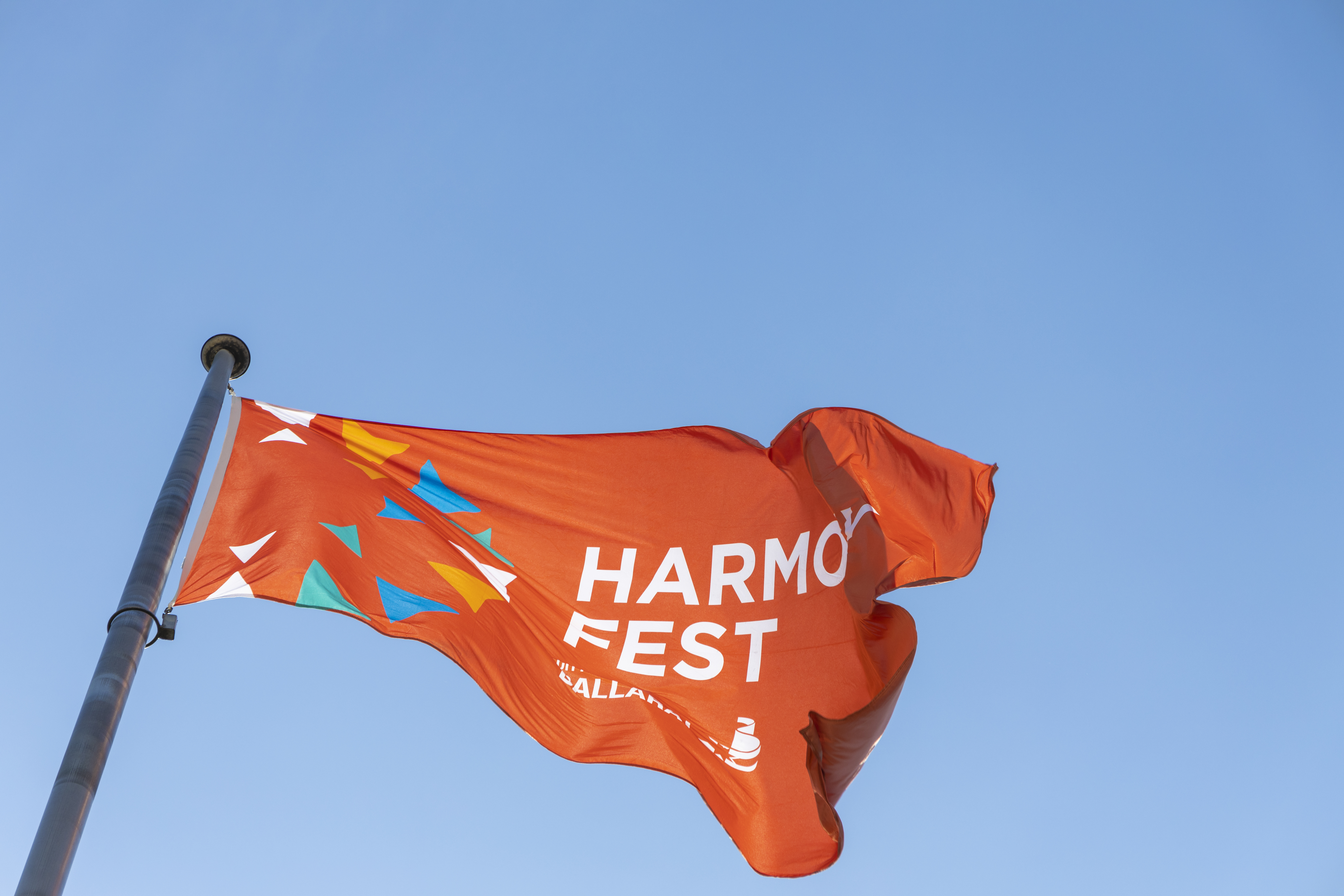 An orange flag with Harmony Fest text flying against a clear blue sky