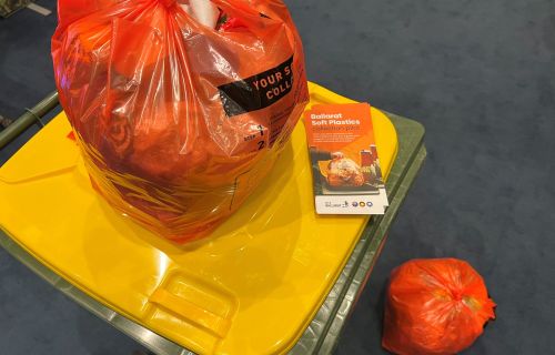 A soft plastics bag sits on top of the recycling bin