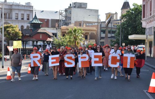 People holding banners spelling out 'Respect' walk down a street with a crowd of people following them.