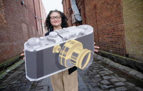 A woman holding a large cardboard cutout of a camera in a Ballarat laneway