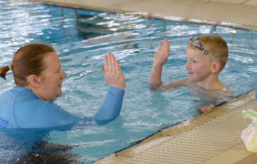 Swim teacher high fives student in pool