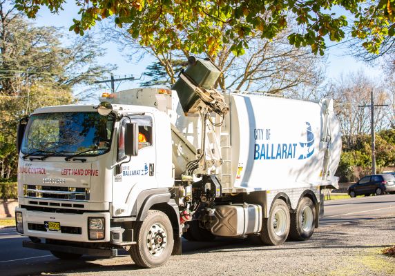 A waste truck lifts a bin, preparing to empty it. 