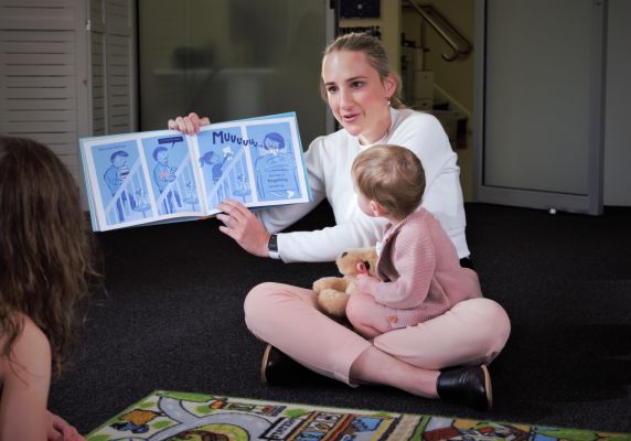 City of Ballarat Deputy Mayor Cr Amy Johnson reads a picture book with a young child in her lap. 