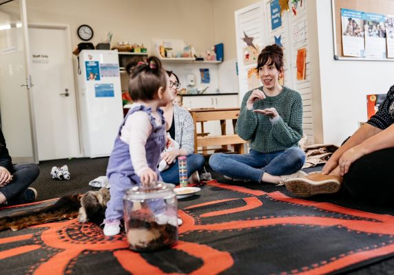 A young child looks back at their mother while sitting on a toy. 