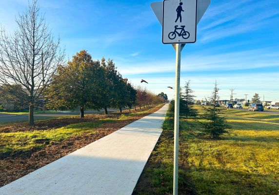 A concrete cycling and walking path sits next to a sign indicating that pedestrians and cyclists can use the path. 