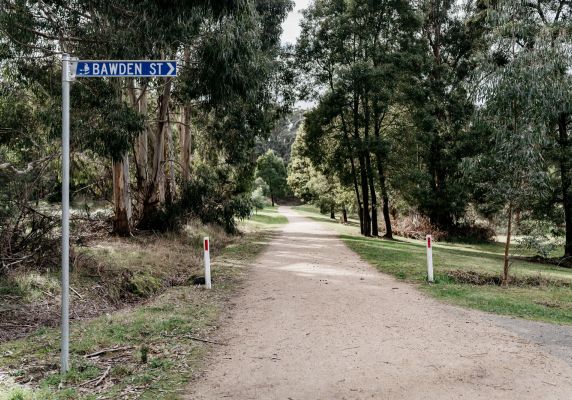 A blue sign on the left says 'Bawden Street'. Next two it there is a tree-lined track. 