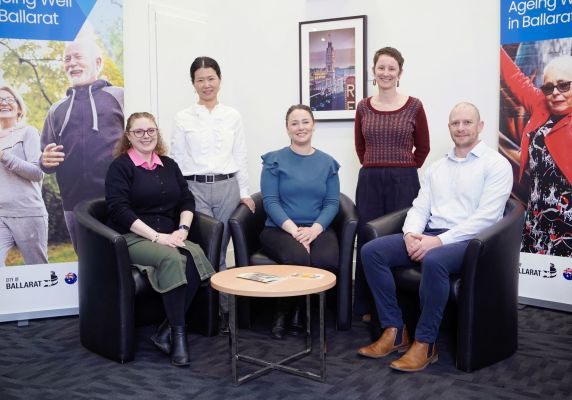 Five people, four women and one man, pose for a photo in front of banners that say 'Ageing Well in Ballarat'. 