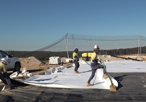 Workers roll out geotextile material at the landfill