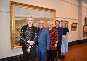Art Gallery of Ballarat Director Louise Tegart, City of Ballarat Mayor Cr Des Hudson, ACU Campus Dean Ballarat Professor Bridget Aitchison, ACU Senior Lecturer in History, National School of Arts and Humanities Dr Benjamin Mountford and Sovereign Hill Museums Association Head of Collections and Curatorial Lauren Bourke stand in front of a large painting in a gold frame. 
