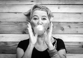 black and white photo of an older woman blowing a bubble with bubble gum